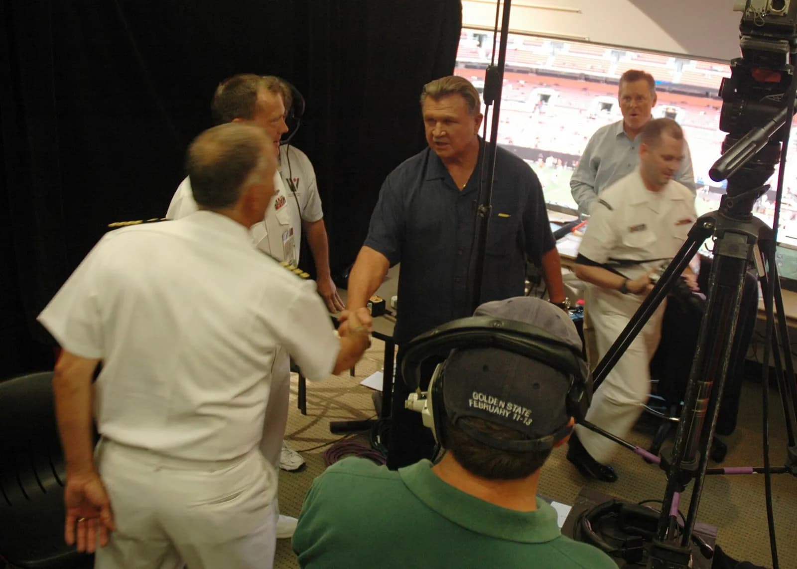 Mike Ditka speaks with sailors in a stadium press booth.