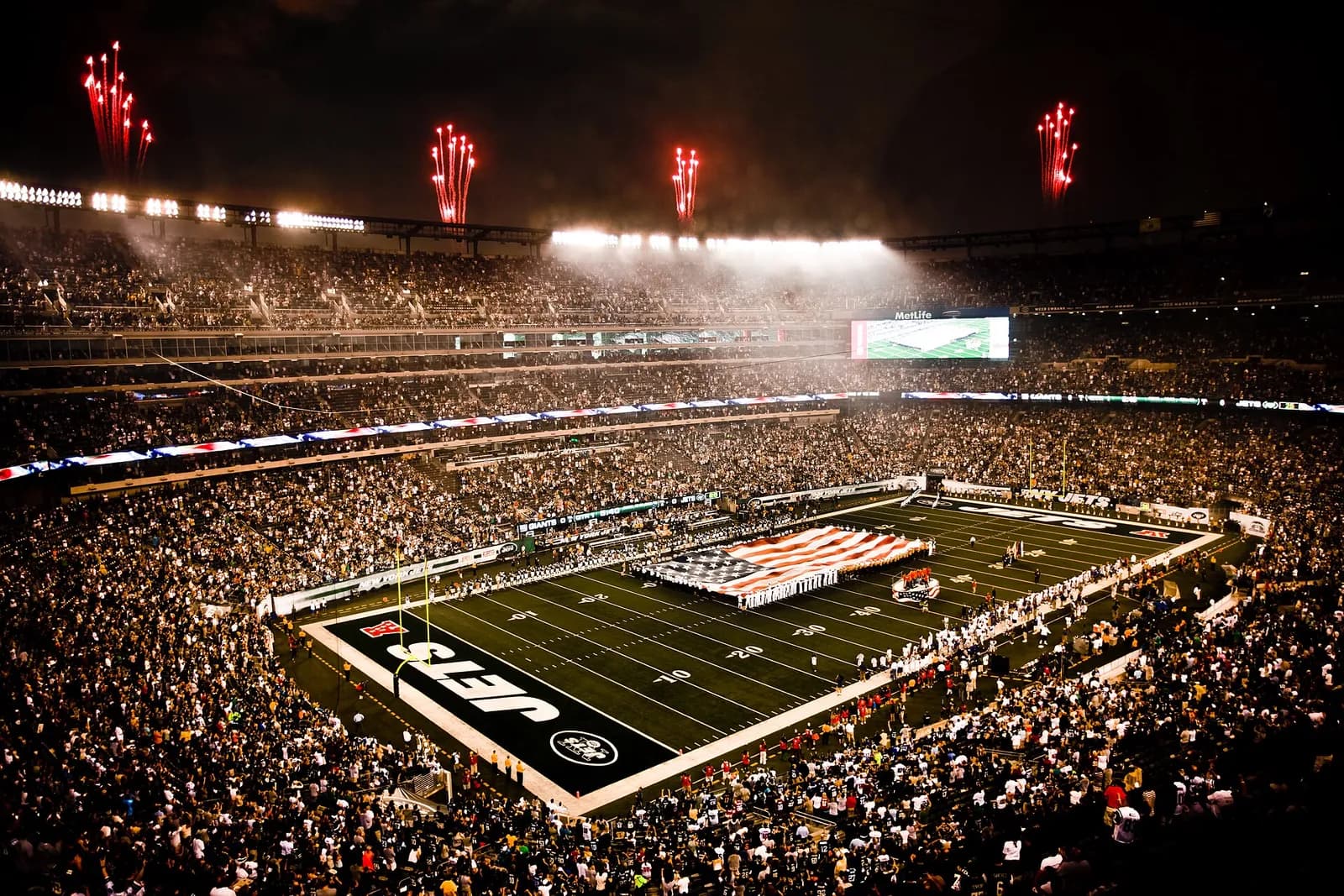 Service members unfurl a large American flag across the field at MetLife Stadium during a pregame ceremony.