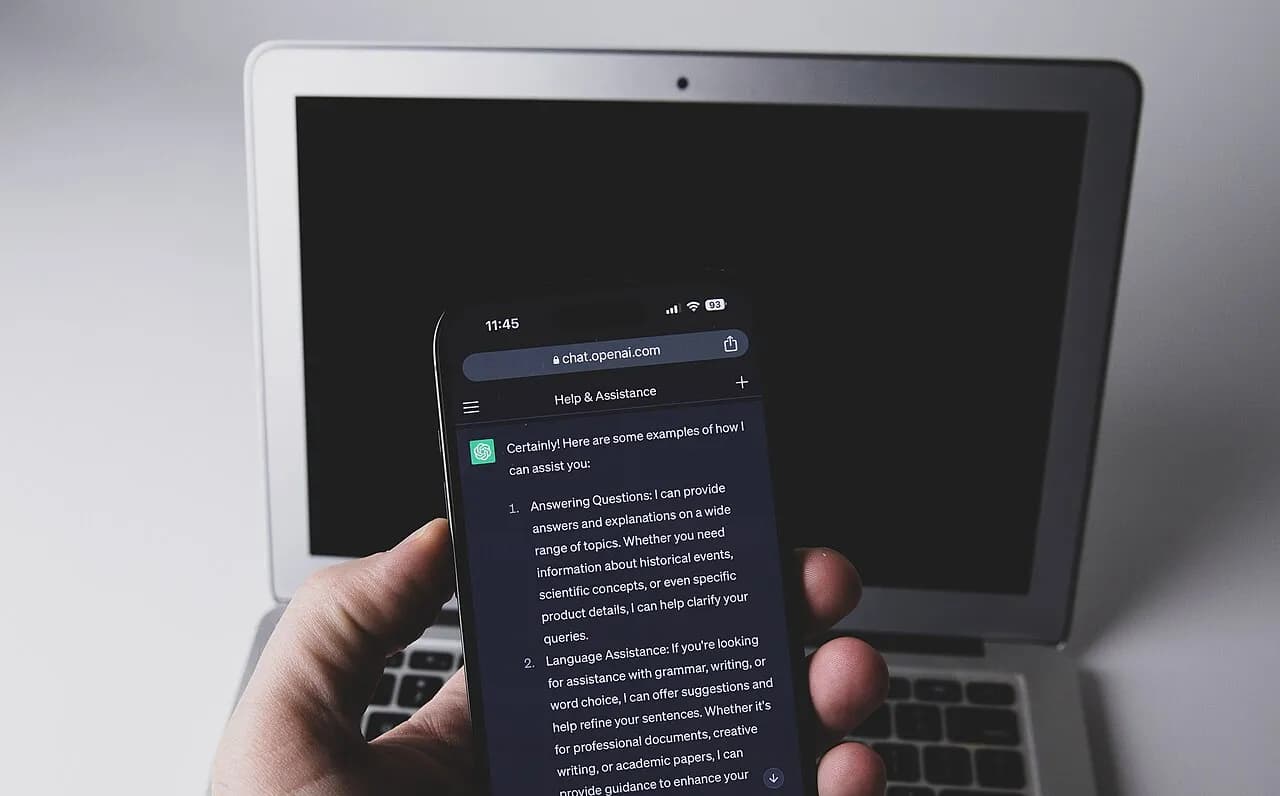 Smartphone displaying ChatGPT in a mobile browser beside a laptop keyboard