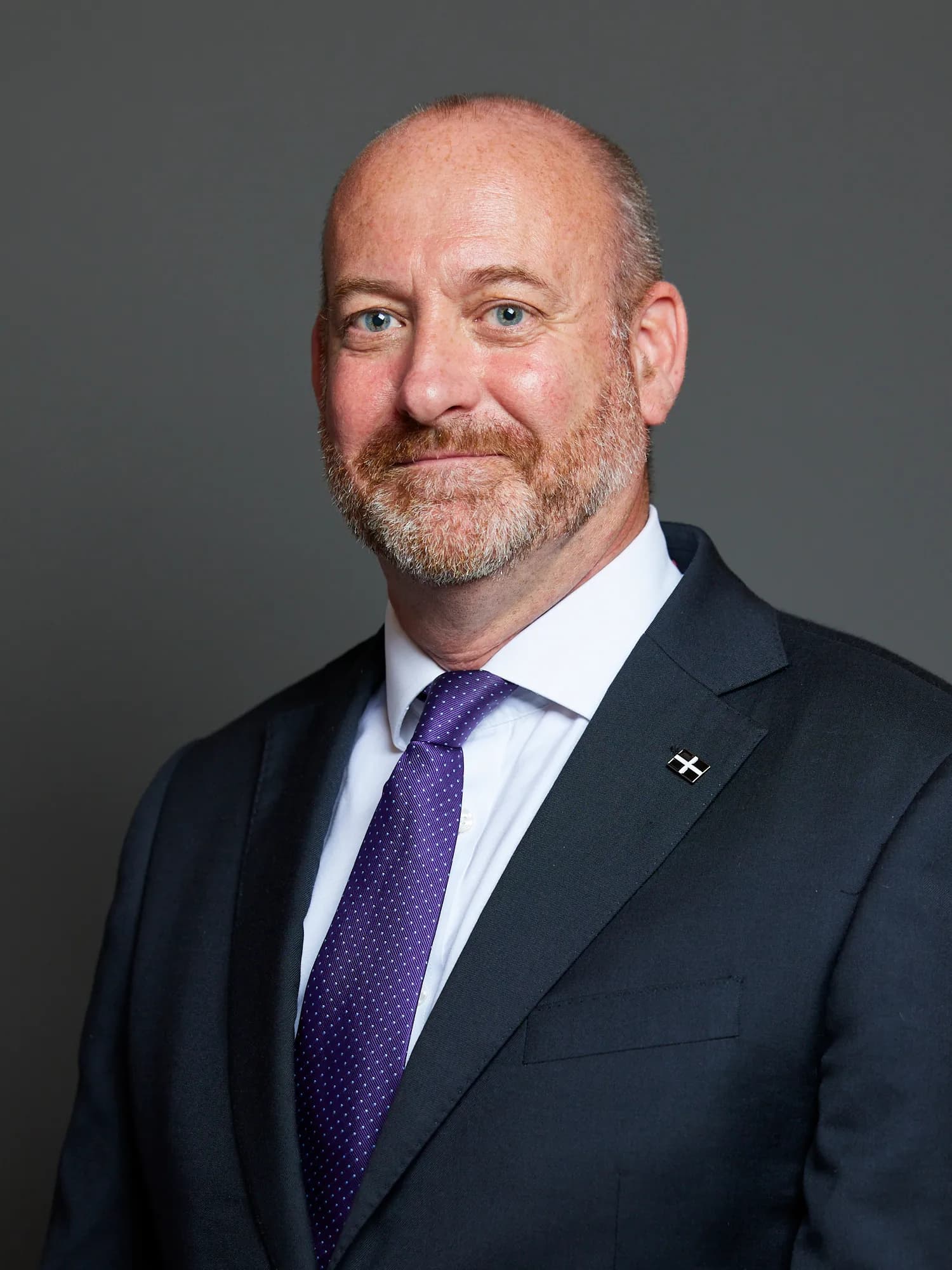 Official portrait of Perran Moon, wearing a dark suit, white shirt and burgundy tie.