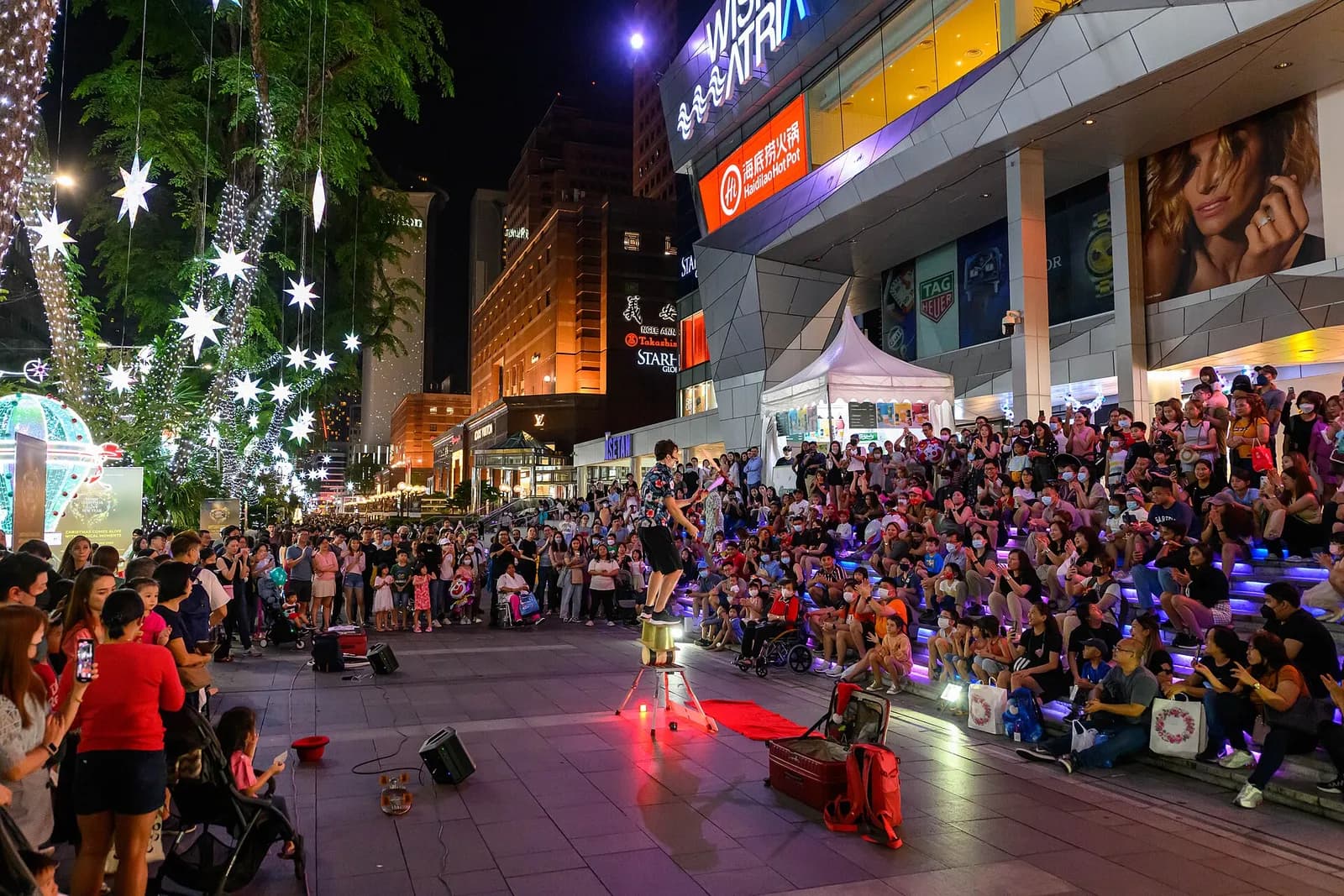 A busker performs for a crowd on Orchard Road at night.