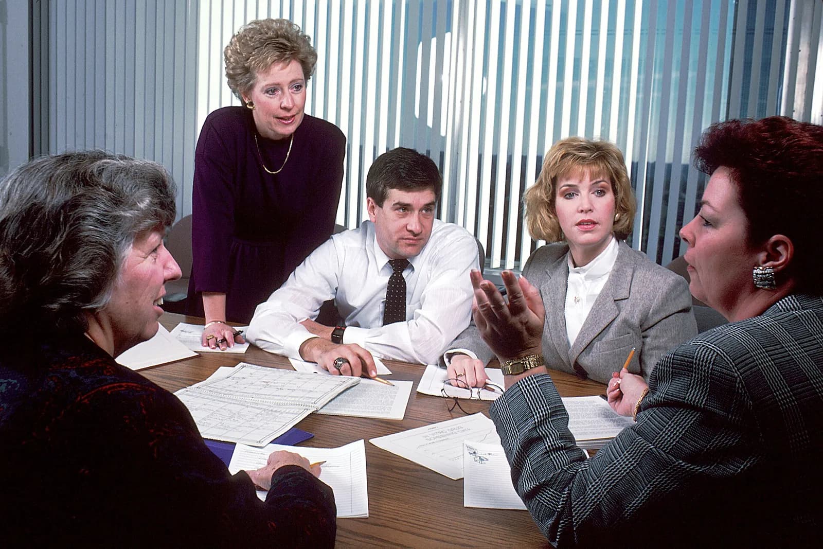 Five people sit around an office conference table discussing a manuscript.
