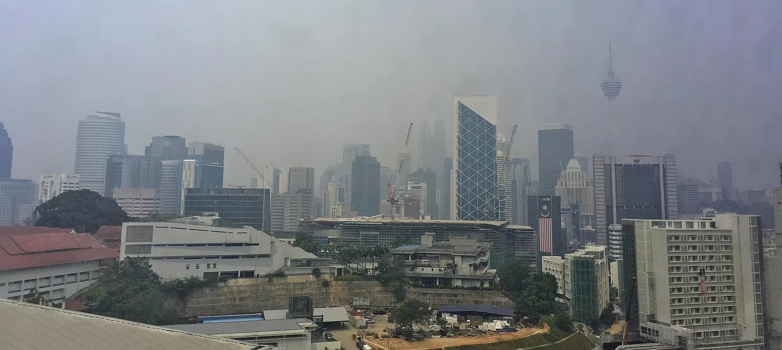 Kuala Lumpur skyline partly obscured by haze, with the Petronas Towers barely visible.