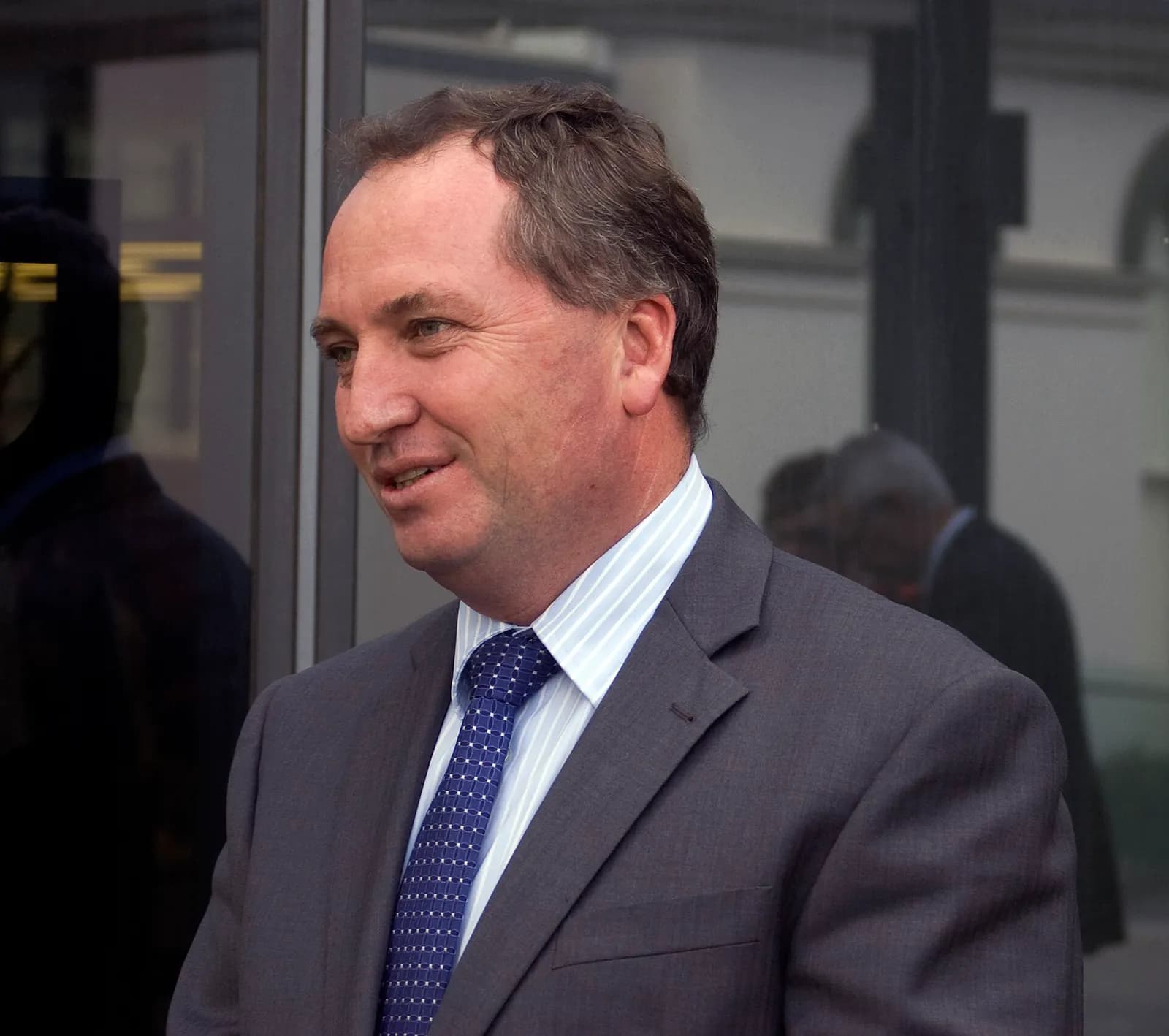 Barnaby Joyce, wearing a suit and tie, speaks with local media outside a building.