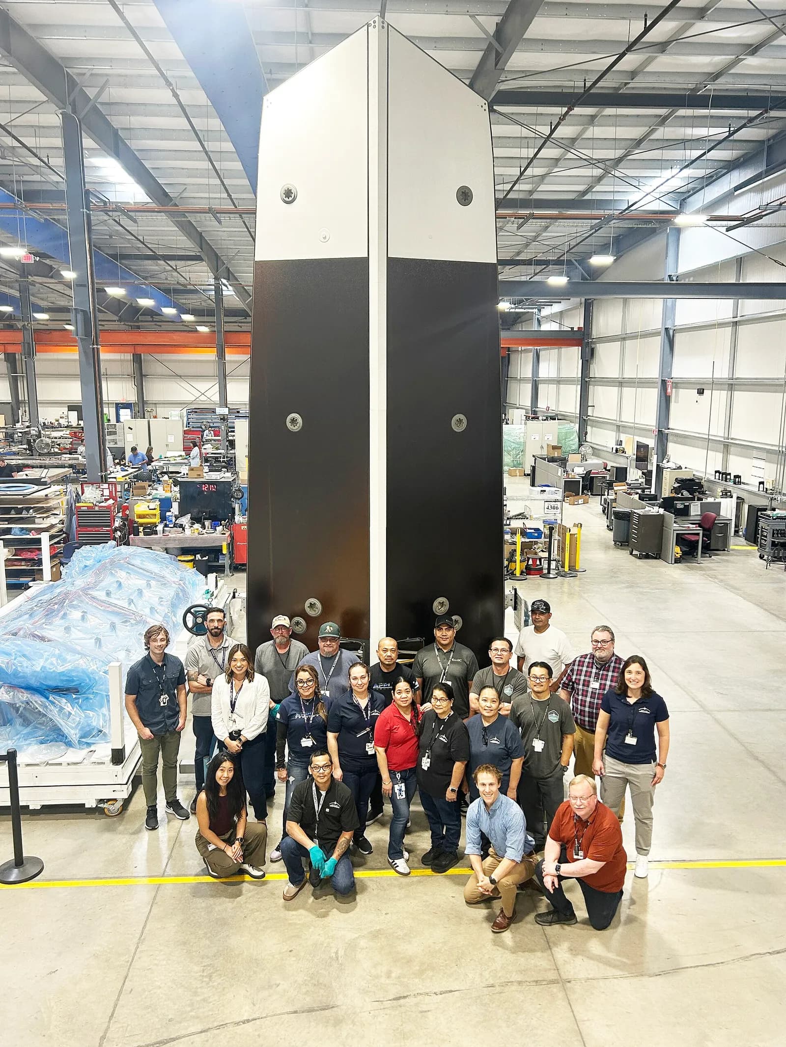 NASA’s NEO Surveyor sunshade towers above a fixture, with technicians and engineers standing in front of it.