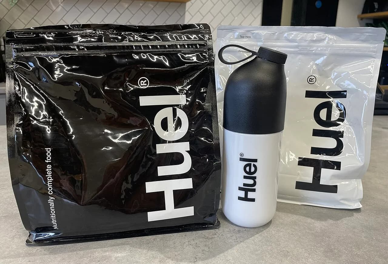 Pouch of Huel Powder Black Edition beside a Huel shaker