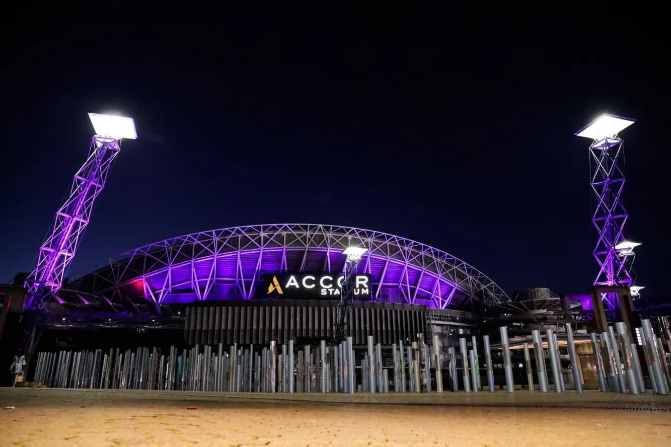 Accor Stadium illuminated purple at night.