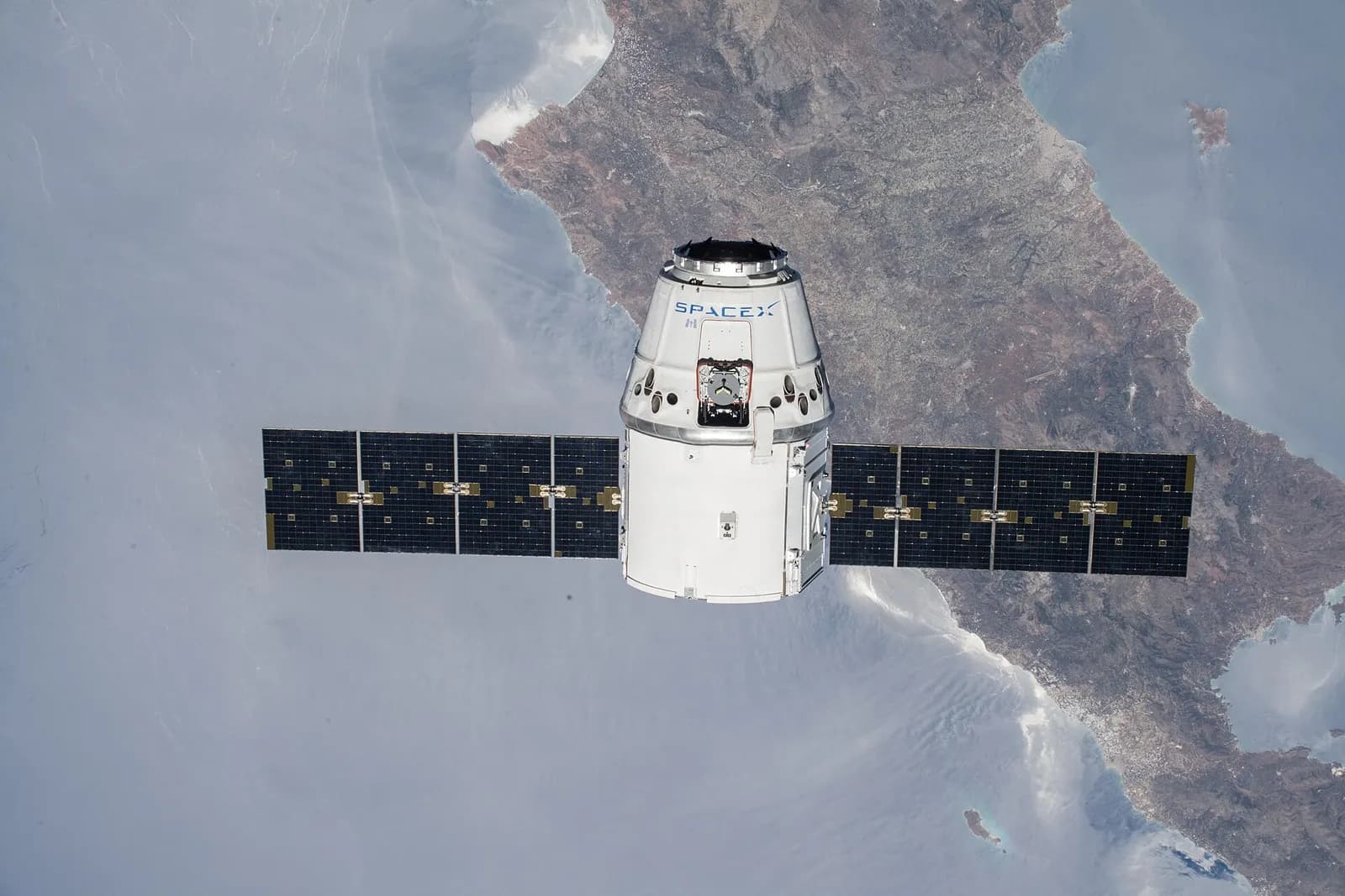 A SpaceX Dragon cargo spacecraft approaches the International Space Station above Earth.