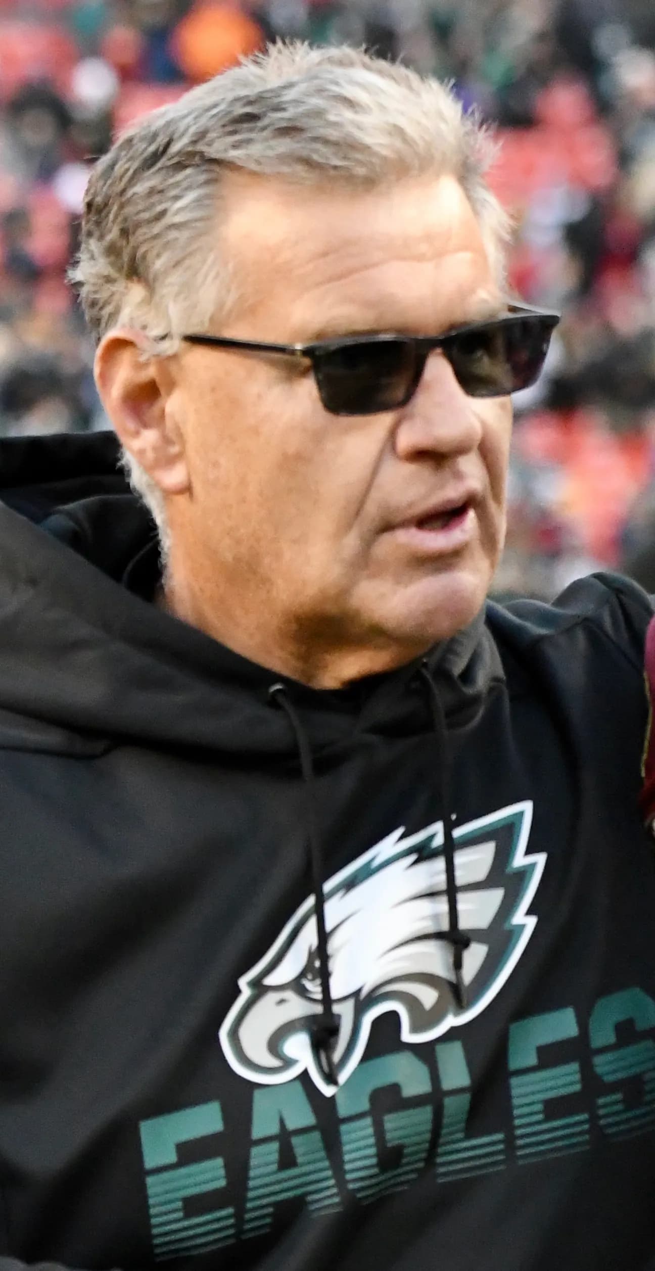 Close-up of a grey-haired man in dark sunglasses and a black Philadelphia Eagles hoodie with the team logo and name on the front.