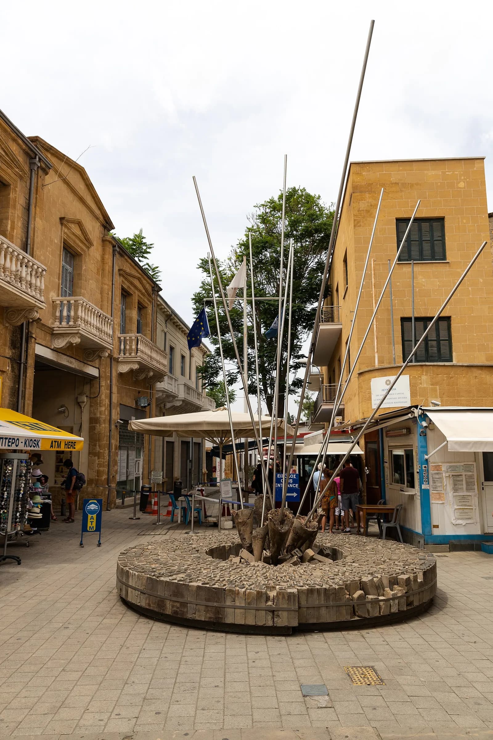 Ledra Street crossing point in Nicosia, Cyprus, with barriers, flags, nearby buildings and people.