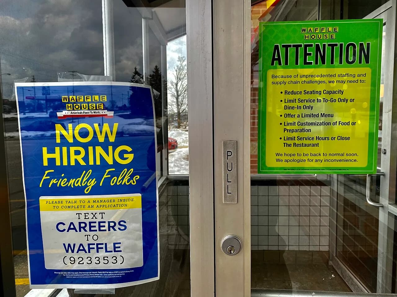 Now Hiring sign beside staffing and supply notices at a Waffle House entrance in Ohio