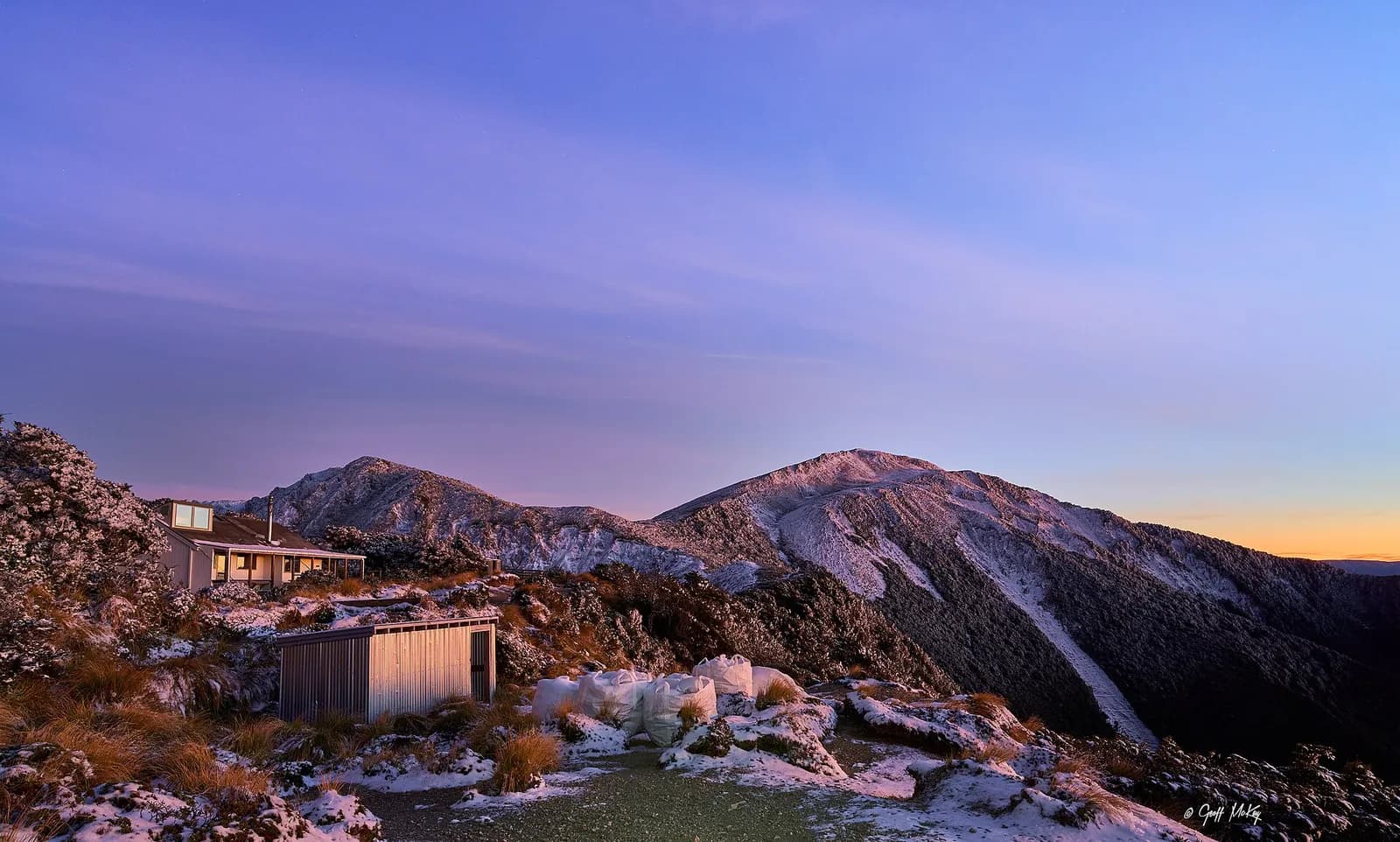 Sunrise Hut with a woodshed and firewood in the foreground, and Armstrong Saddle behind it.
