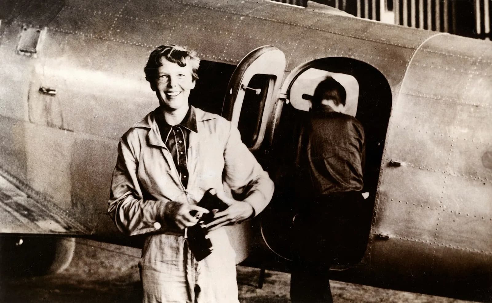 Amelia Earhart stands beside her Lockheed Electra as Fred Noonan gets into the plane.