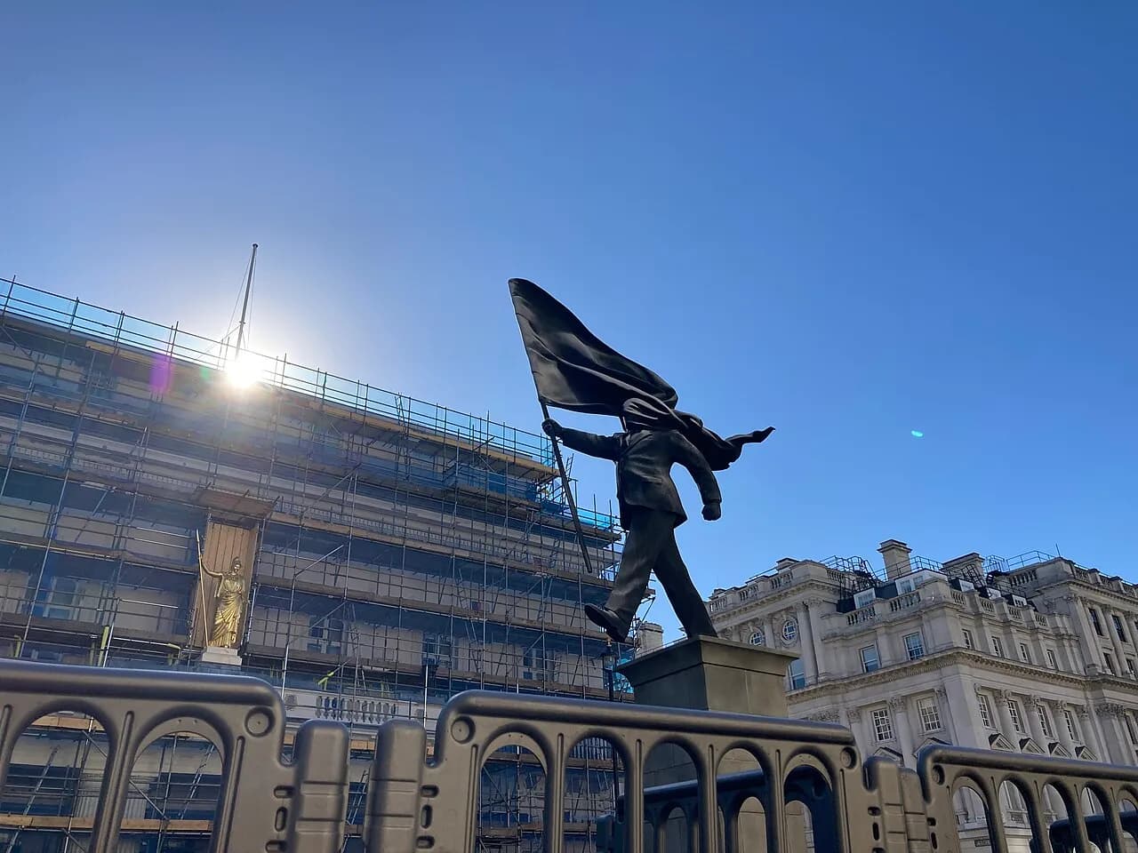 A suited figure strides from a plinth while a large flag obscures its face at Waterloo Place, London.