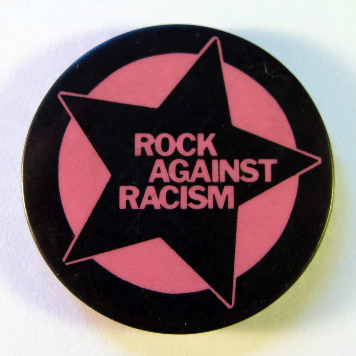 A black and pink Rock Against Racism badge with a star and the words ‘Rock Against Racism.’