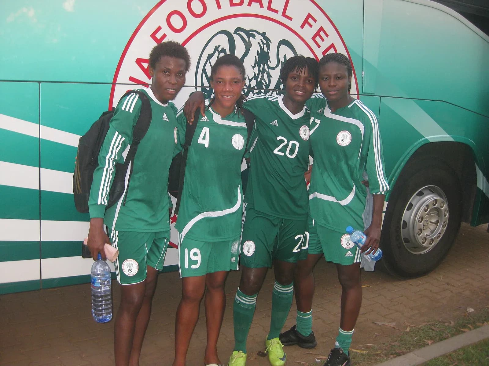 Four Super Falcons players pose together beside a team bus after training.