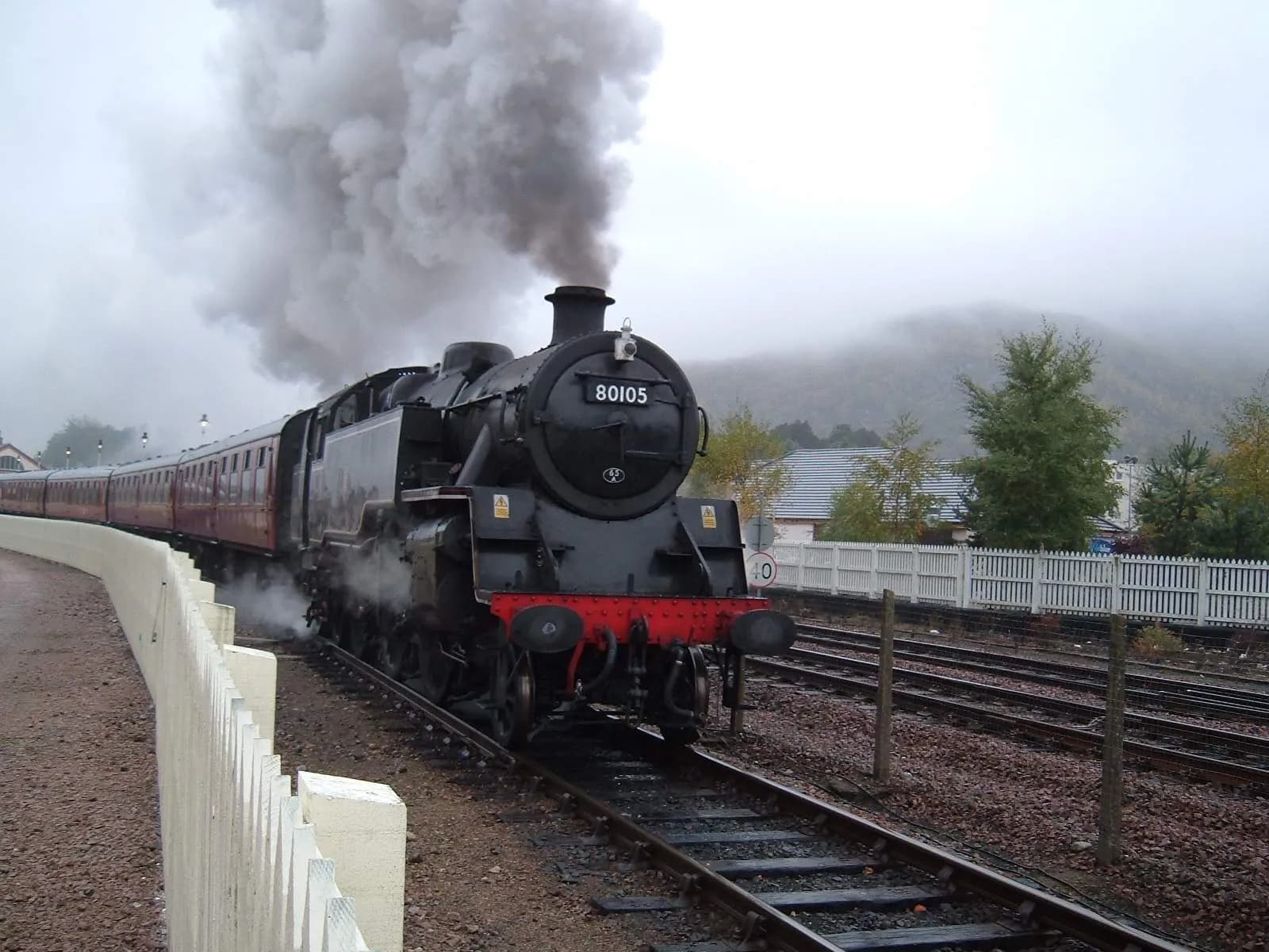 Train departing Aviemore station on the Strathspey Railway, with a hill behind it