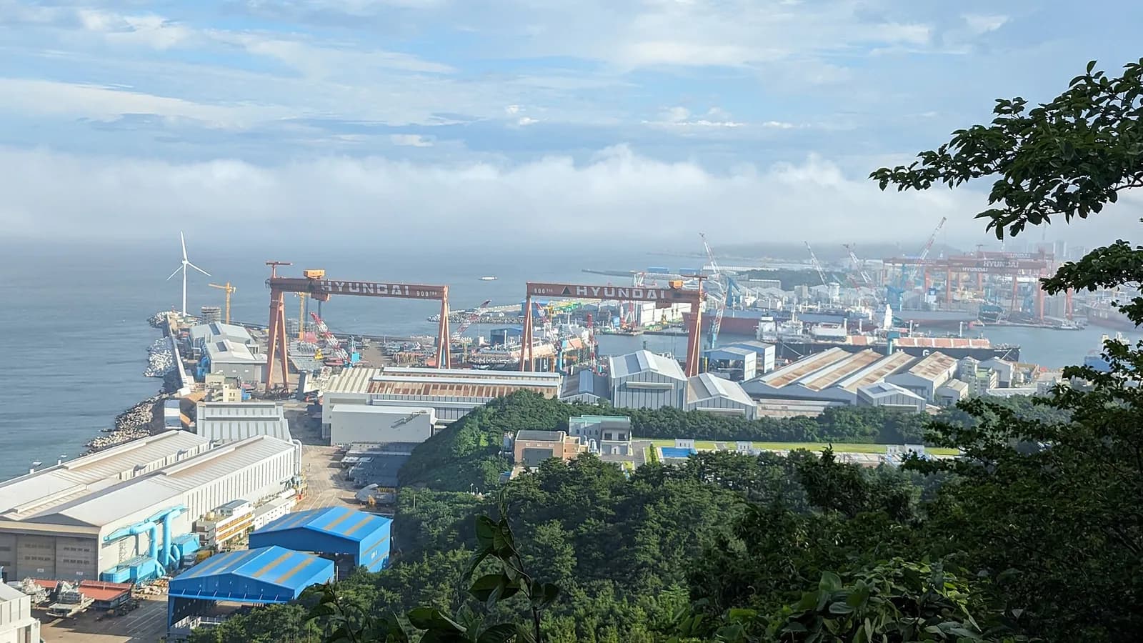 Red gantry cranes at HD Hyundai Heavy Industries’ Ulsan shipyard, viewed from the coast.