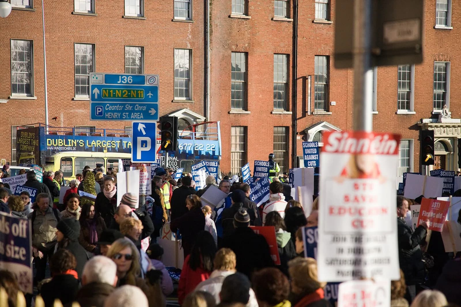 A crowd of demonstrators with Schools United signs gathers on a Dublin street beneath red-brick buildings.