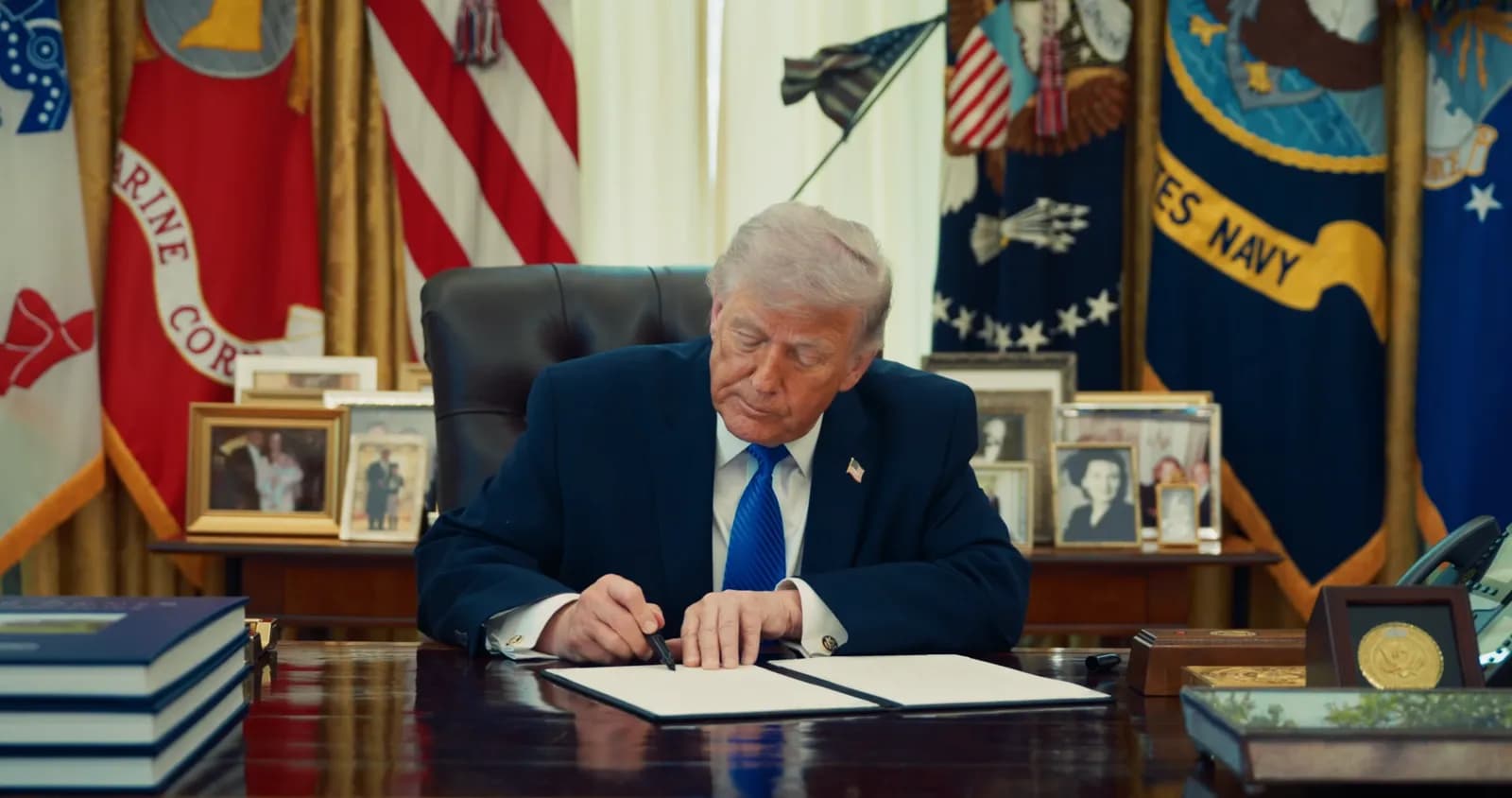 U.S. President Donald Trump signs an executive order at a desk in the Oval Office.