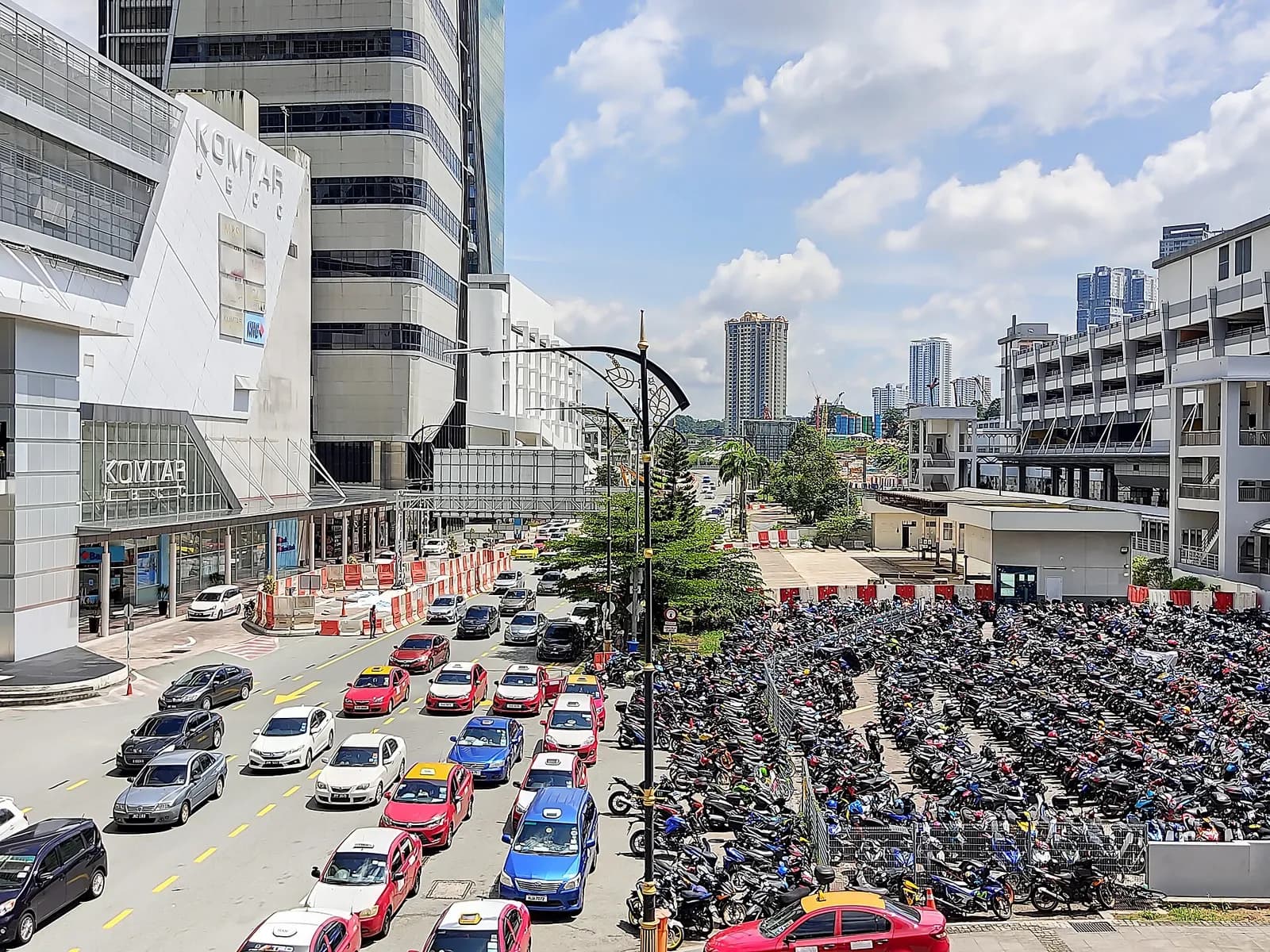 A view of the KOMTAR area in Johor Bahru, with a busy road and a large motorcycle parking area between commercial buildings.