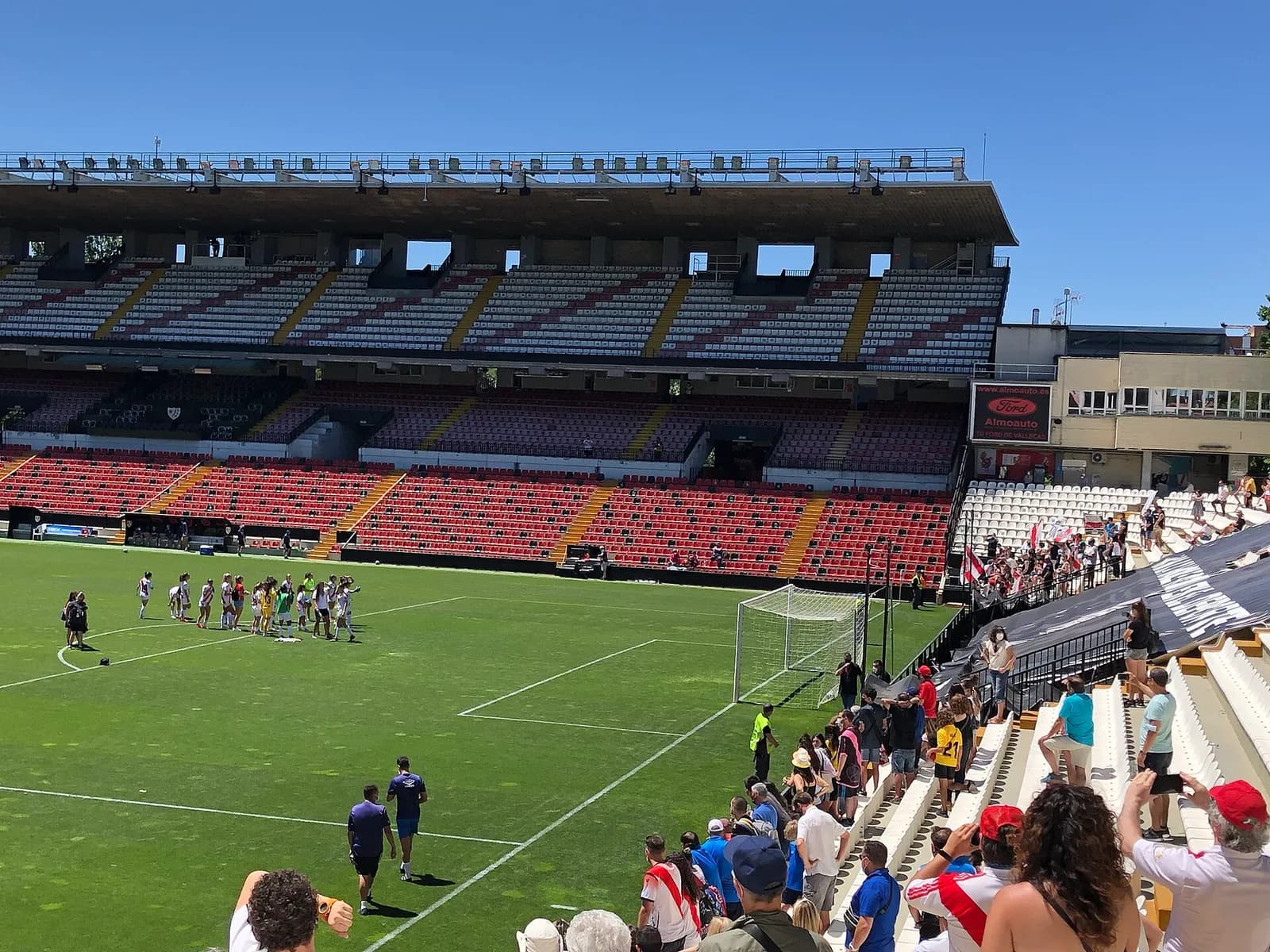 View from inside Estadio de Vallecas, with the football pitch in the foreground and the stadium stands beyond.