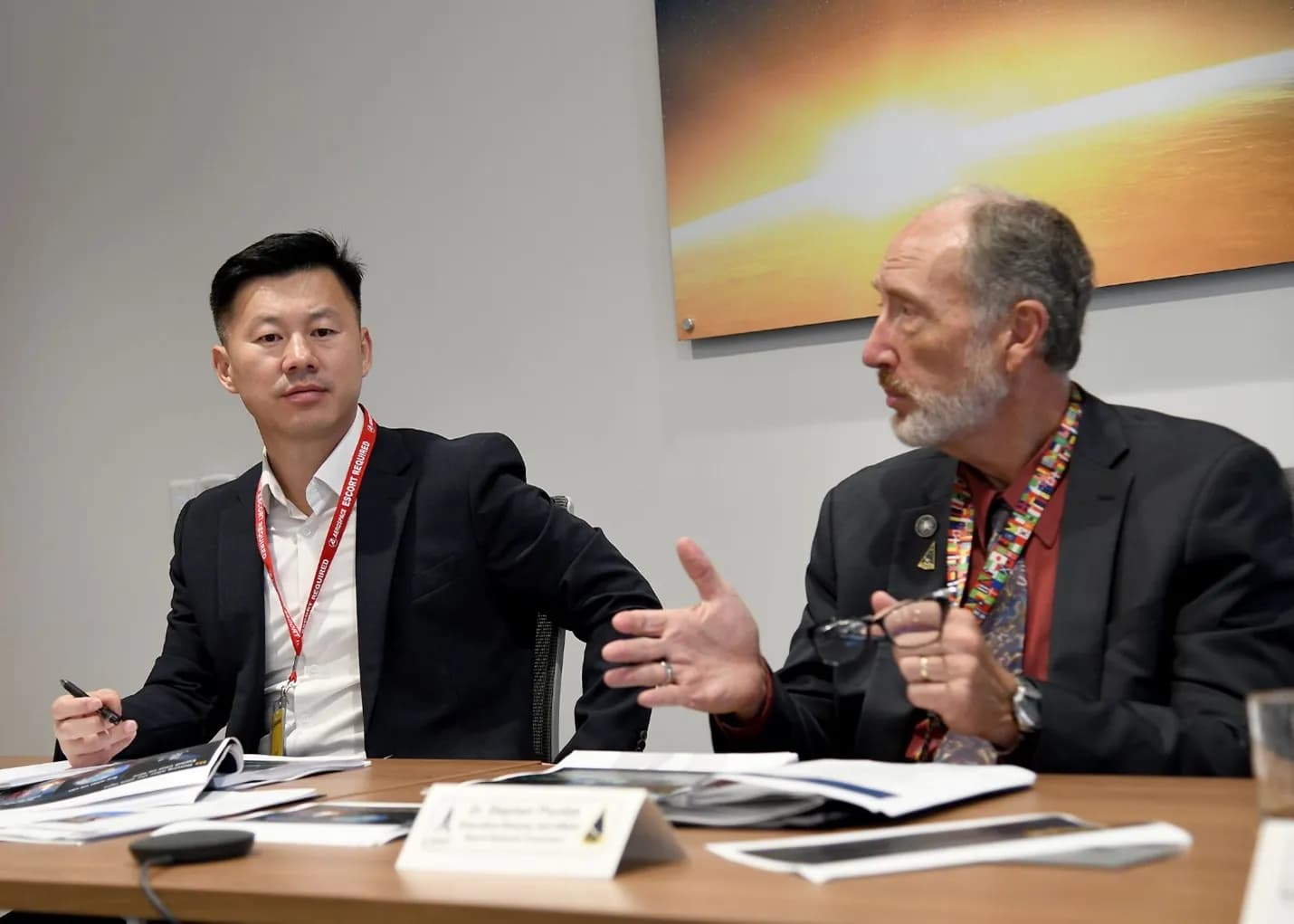 Col. Hyunjin Park sits at a meeting table and listens as U.S. Space Force official Dr. Steve Pluntze speaks and gestures.