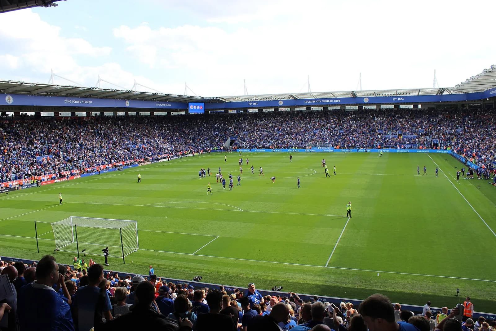 A football match underway at King Power Stadium, with spectators filling the stands.