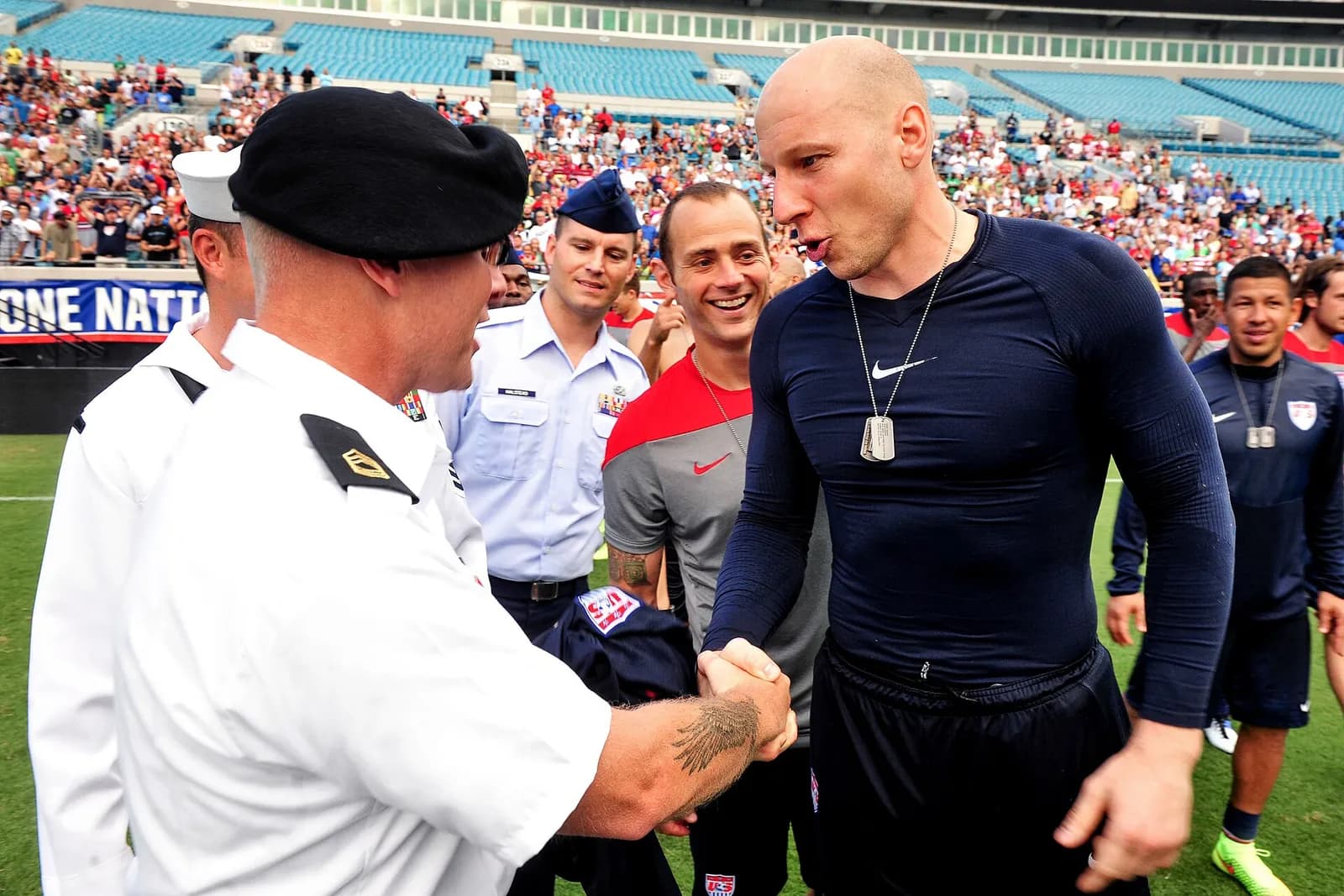 A U.S. servicemember shakes hands with a member of the U.S. Men's National Soccer Team at a stadium ceremony.