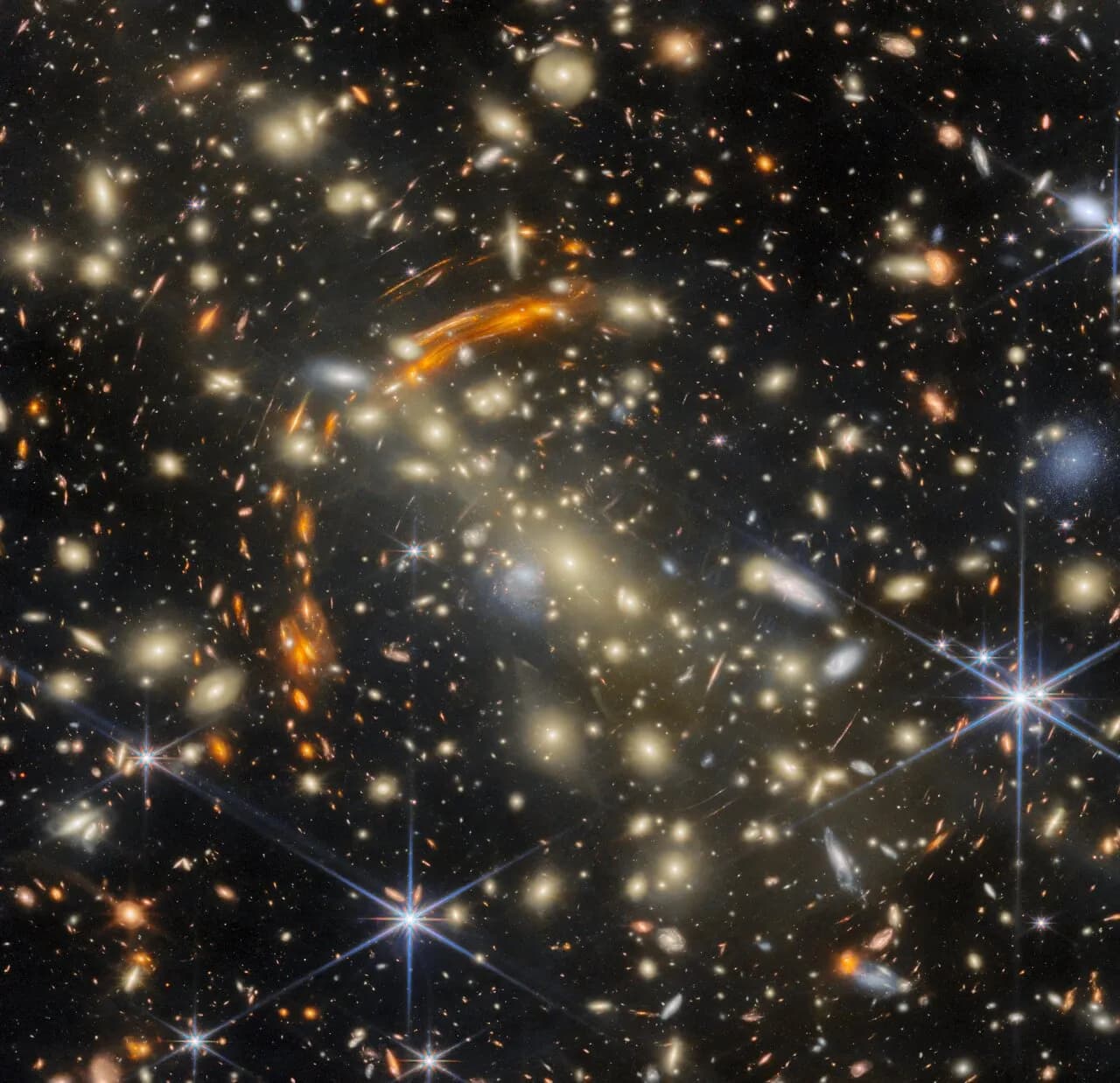 Golden galaxies in cluster MACS J0454.1-0300, surrounded by orange arcs of more distant galaxies whose light is bent by the cluster's gravity.