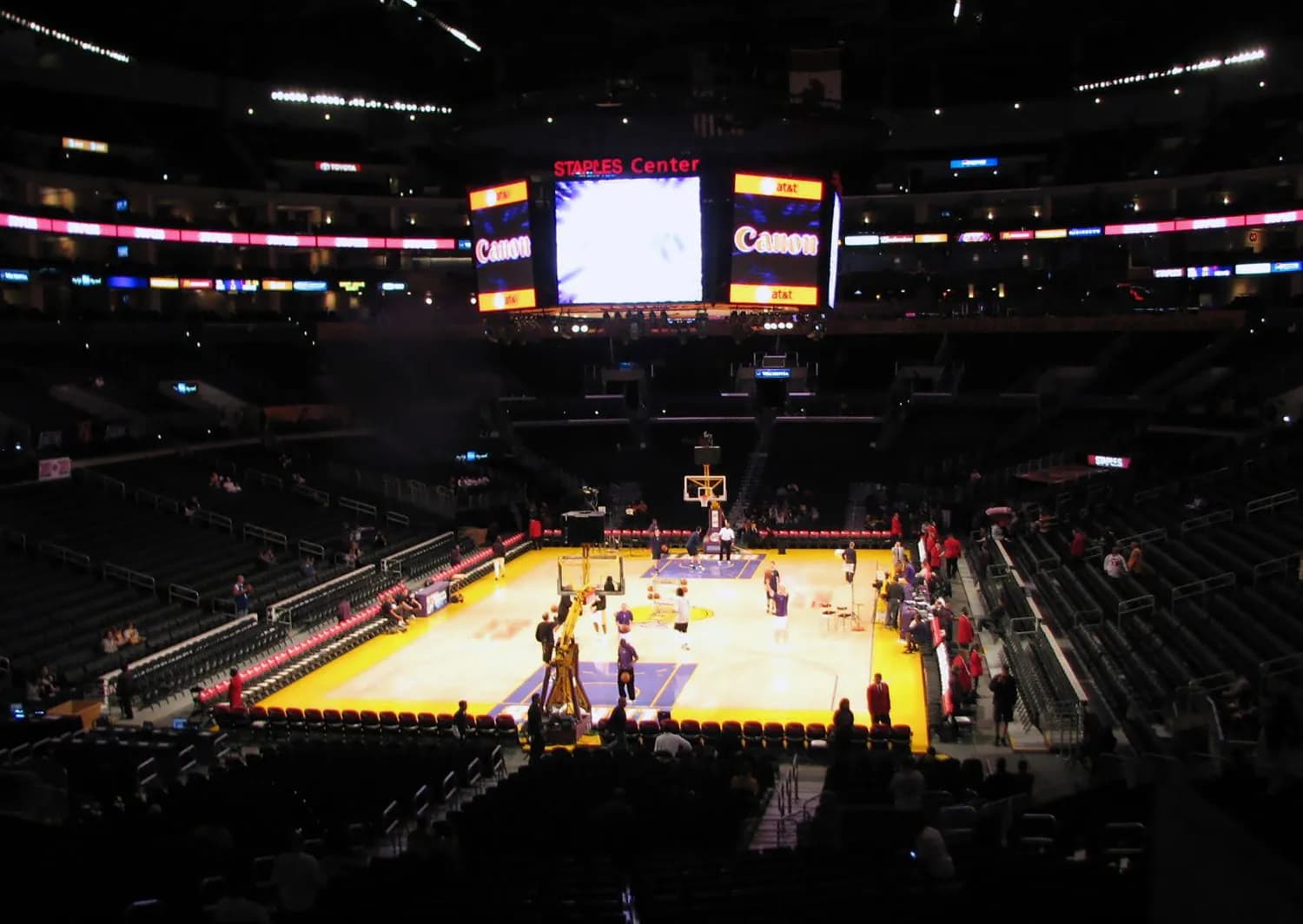 Basketball court inside Staples Center, with people on the court and mostly empty spectator seats.