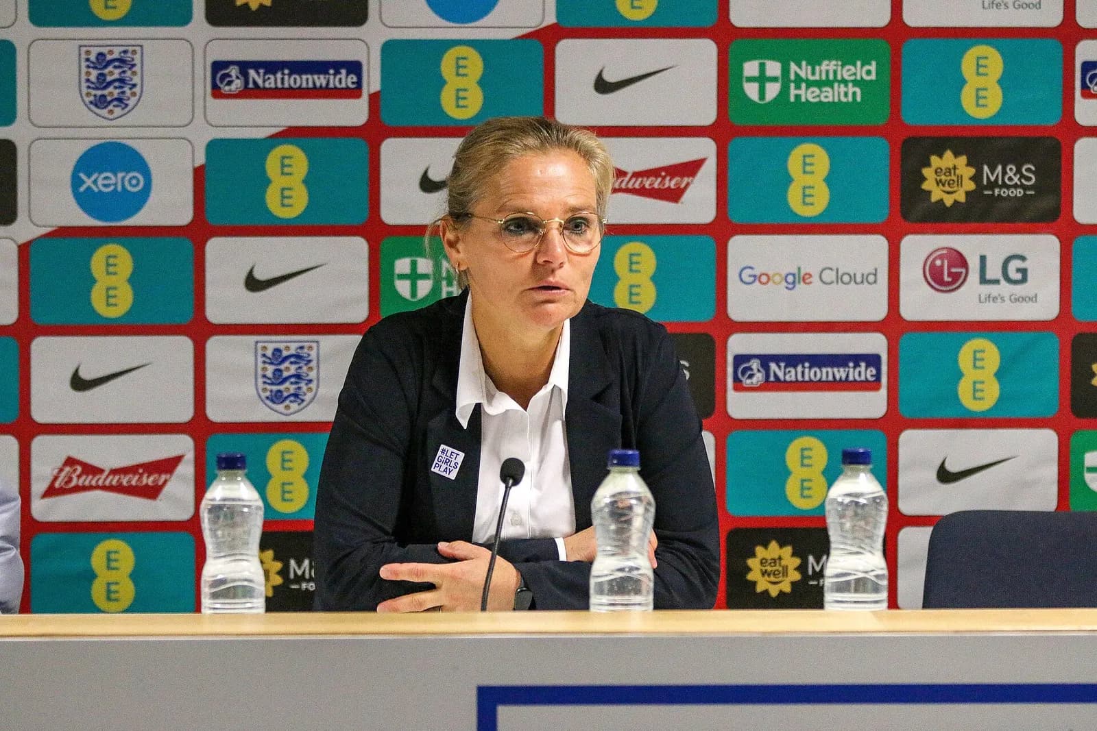 Sarina Wiegman seated at a press conference in front of a sponsor backdrop.