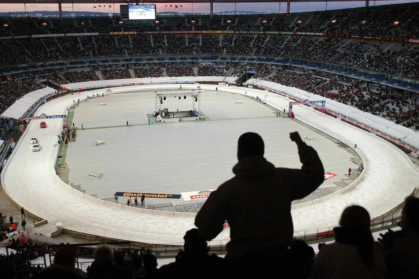 Interior view of Stade de France in Saint-Denis, France, with an indoor motorsport track and spectators in the stands.