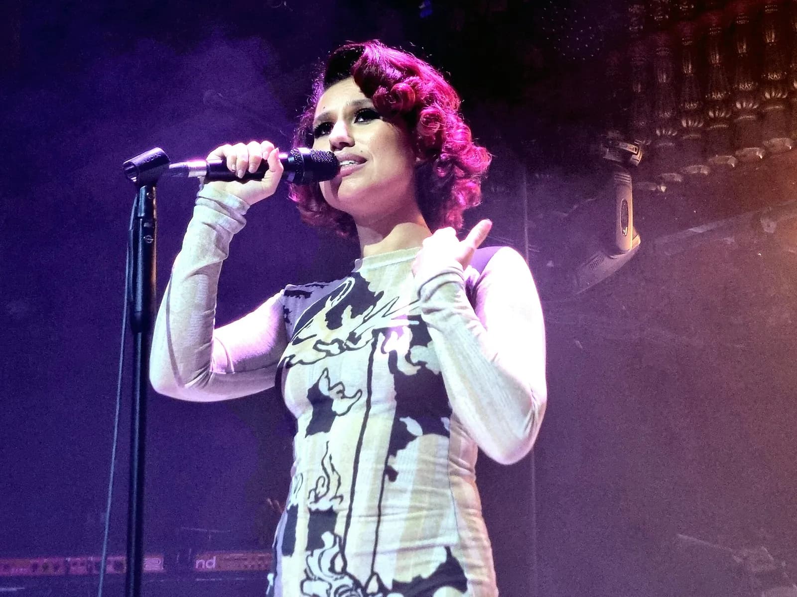 Raye sings into a microphone while performing onstage.
