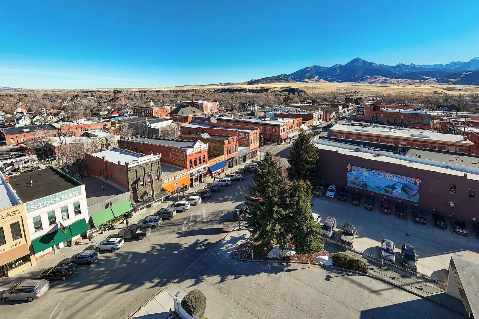 Aerial view of downtown Livingston, Montana, with buildings and streets below and mountains in the distance.
