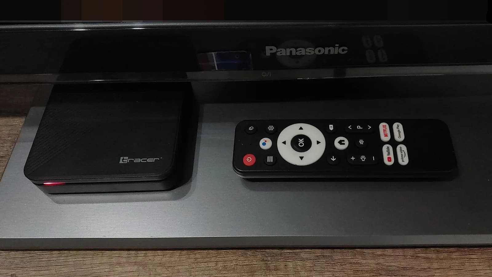An Android TV-based Tracer set-top box beside its remote control and a Panasonic television.
