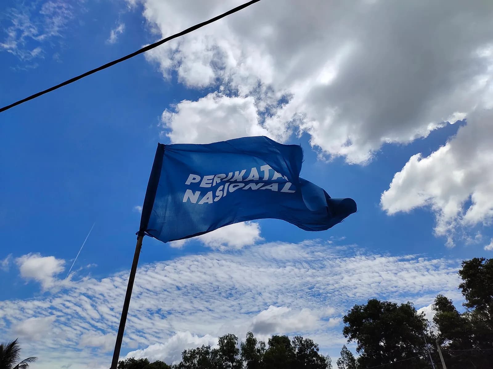 A Perikatan Nasional flag flying against a cloudy sky.