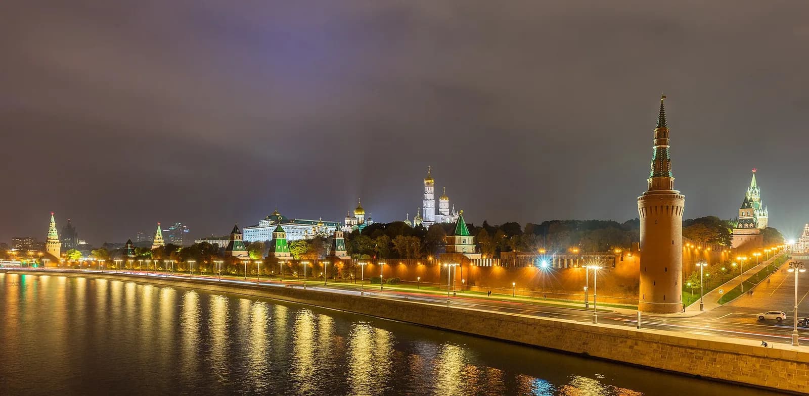 The Moscow Kremlin illuminated at night, with its walls and towers reflected in the river.