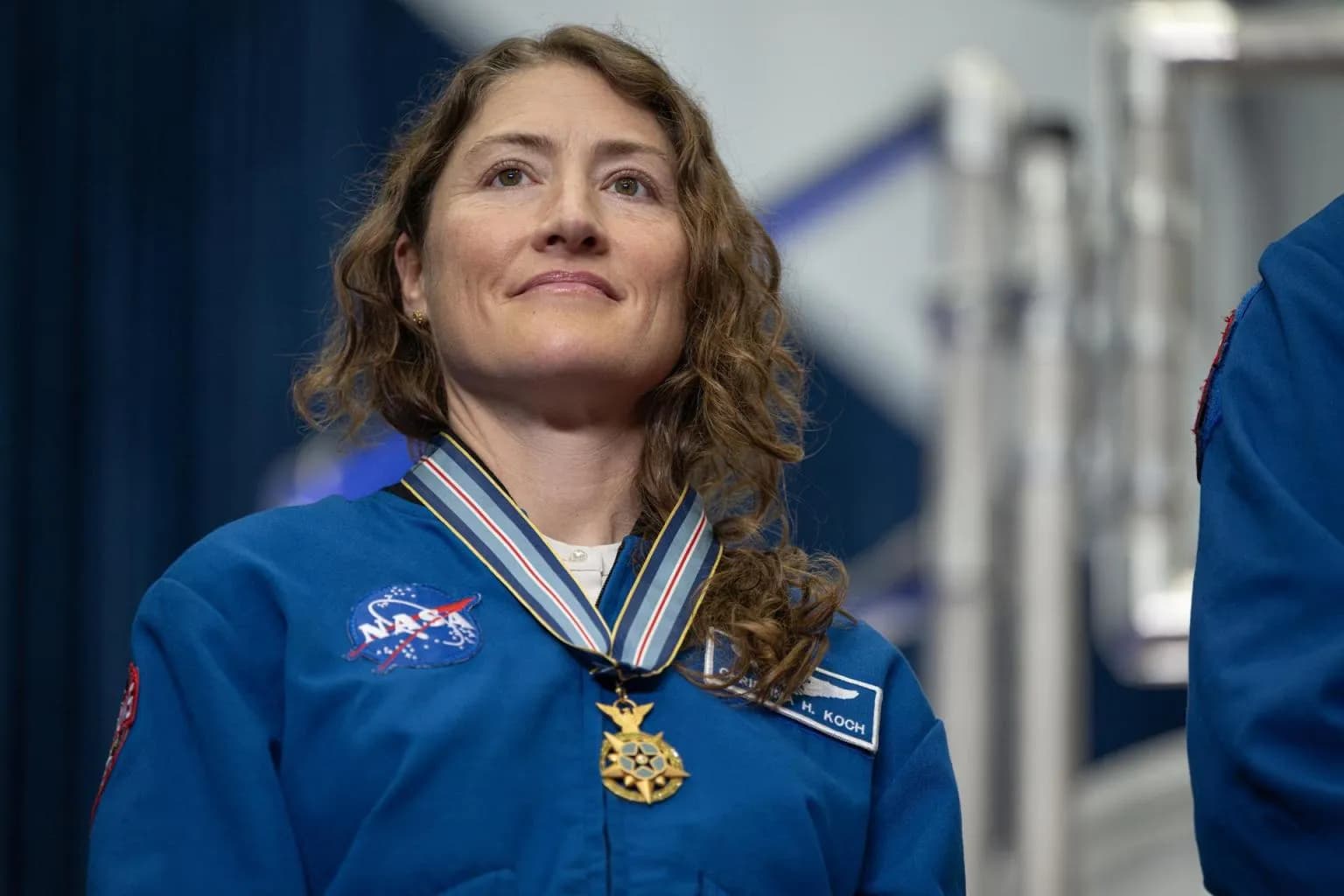 NASA astronaut Christina Koch smiles in a blue flight jacket while wearing her Congressional Space Medal of Honor.