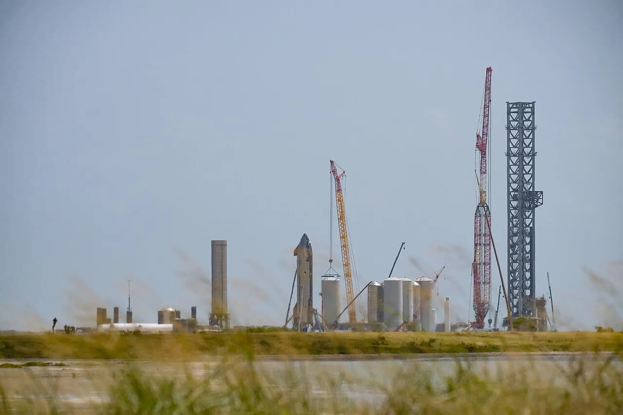 Starship hardware and a launch tower at SpaceX's Starbase facility in Texas, viewed across the water
