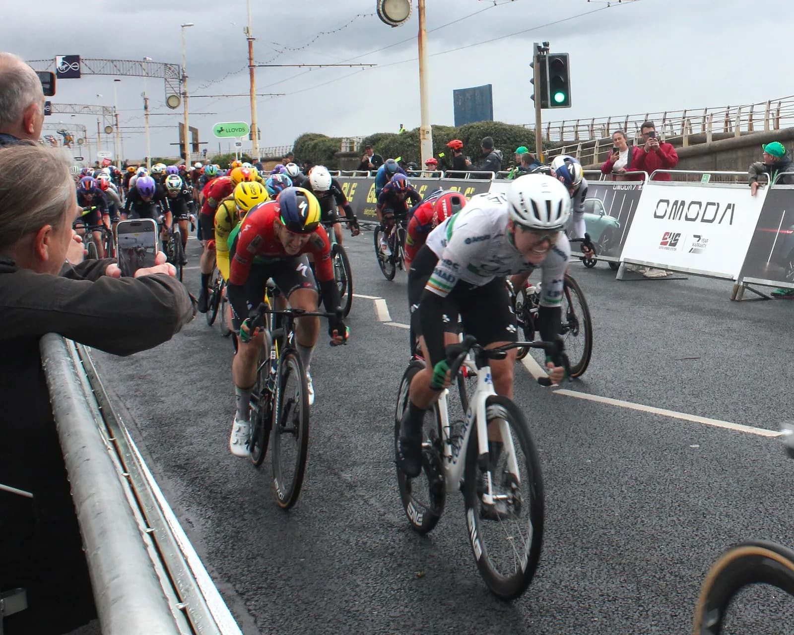 Lara Gillespie in a white Irish cycling jersey races Kim Le Court in a red jersey on a road course.