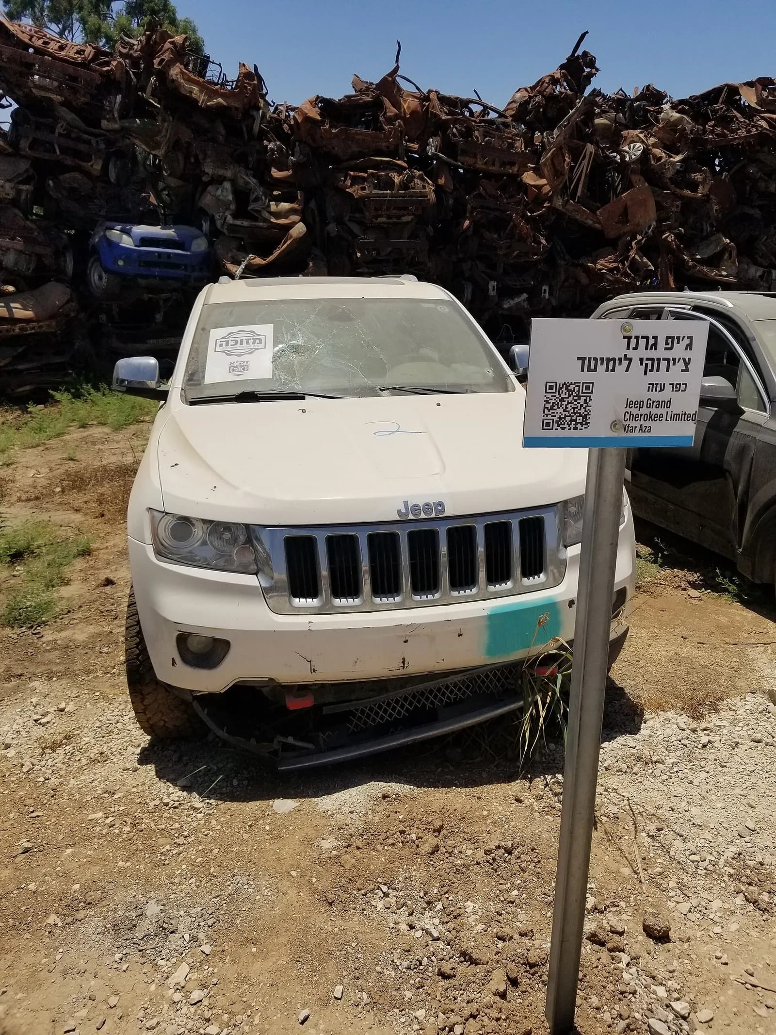 A Zaka vehicle from Kfar Aza with a smashed windshield, displayed among burned vehicles at The Car Wall near Tkuma.