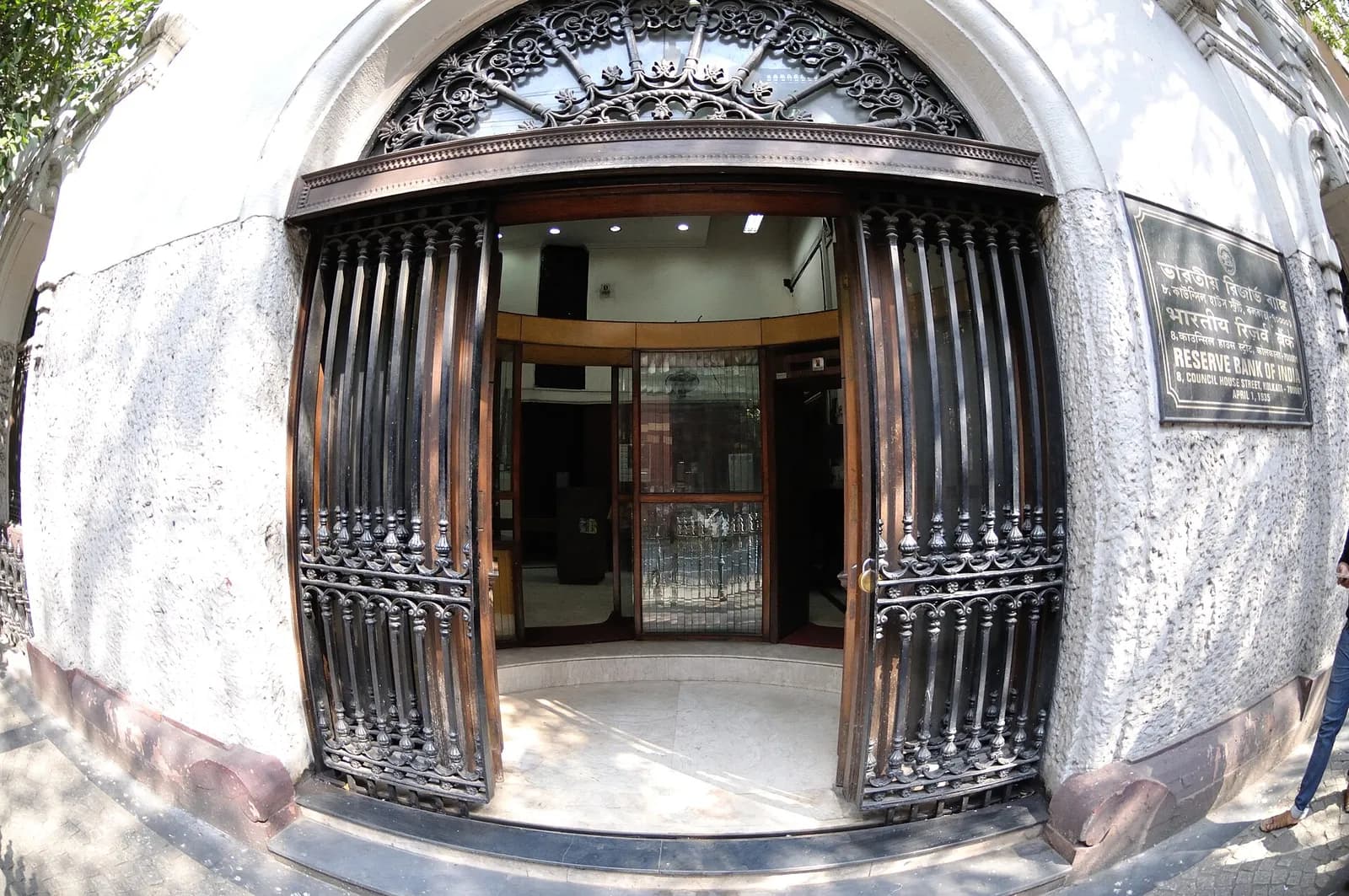 Open black wrought-iron gates at the arched stone entrance of a Reserve Bank of India building, with a dark plaque inscribed 'Reserve Bank of India, 8 Council House Street' on the wall to the right.