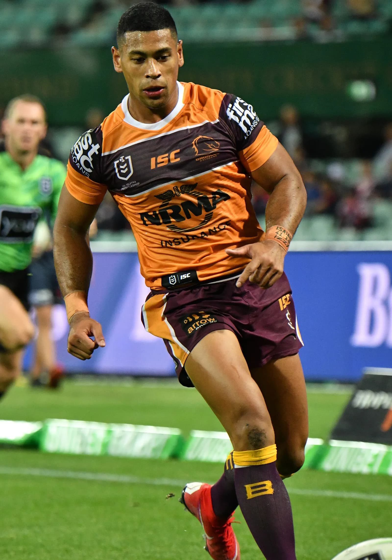 A rugby league player in an orange and maroon Broncos jersey running forward with the ball.