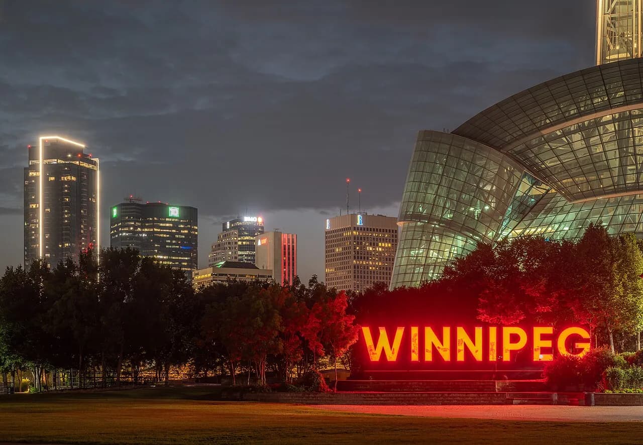 Winnipeg skyline at dusk, with an illuminated WINNIPEG sign in the foreground