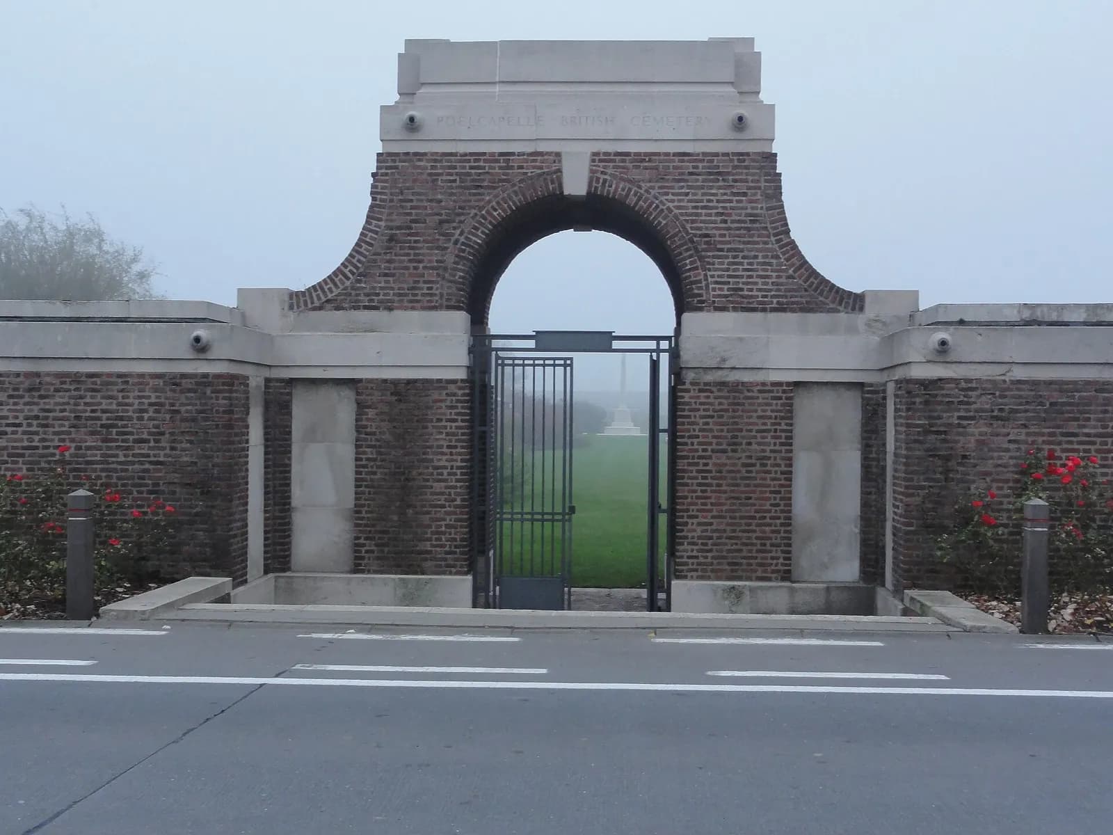 The brick entrance and open metal gate of Poelcapelle British Cemetery.