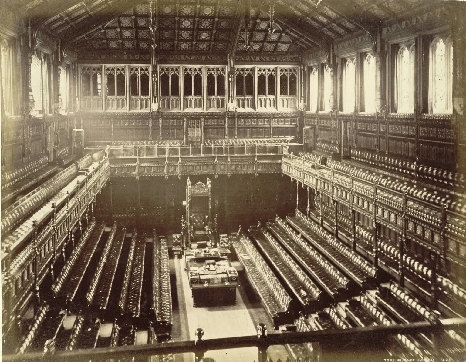 Historic photograph of the House of Commons chamber, with rows of benches facing the Speaker’s chair.