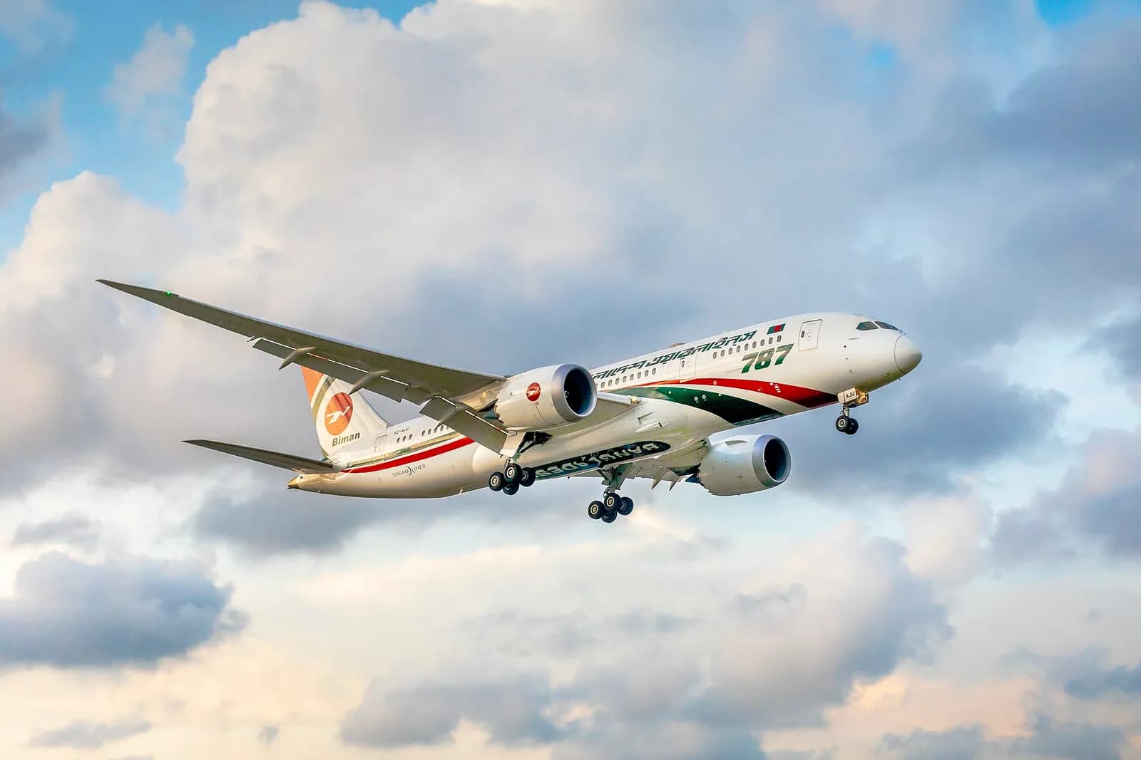 A Biman Bangladesh Airlines Boeing 787 flies with its landing gear extended against a cloudy sky.