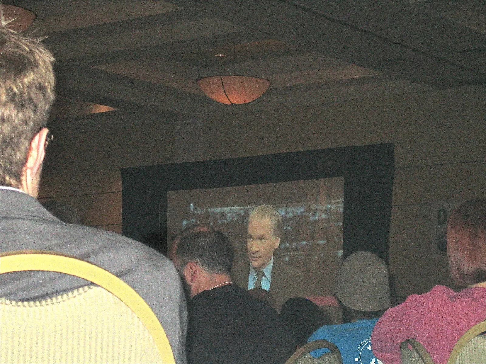 Conference attendees watch Real Time with Bill Maher projected on a large screen.