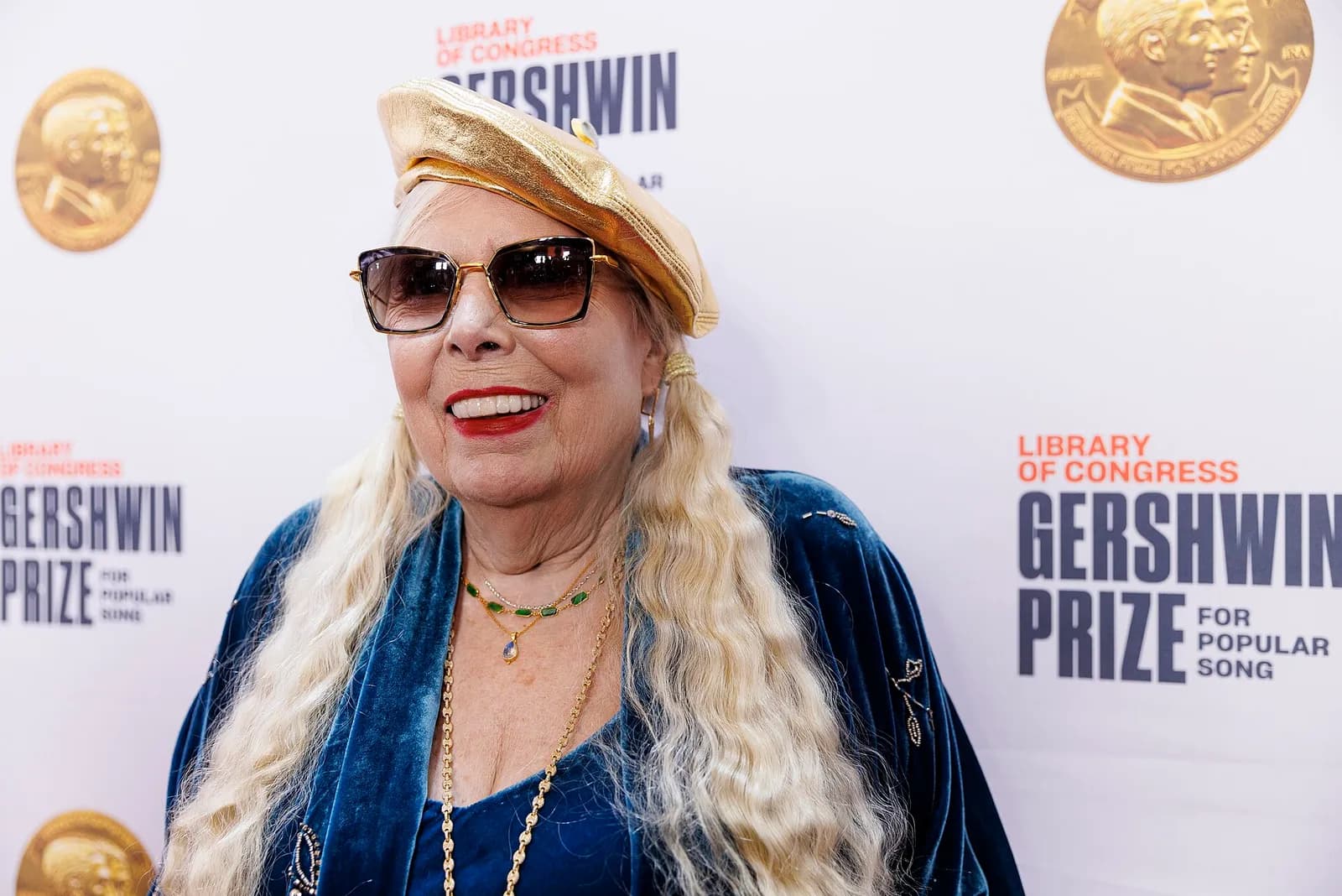 Joni Mitchell speaking to media at a red carpet event.